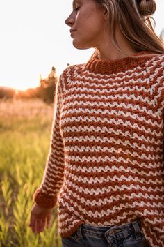 a woman in an orange and white knit sweater stands in a field with her eyes closed