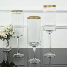 three clear wine glasses with gold rims and flowers in vases next to each other