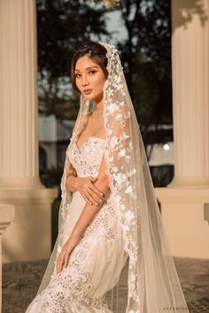 a woman in a white wedding gown and veil posing for the camera with her hands on her hips