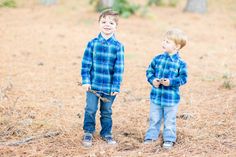 two young boys standing next to each other in a field with trees and grass behind them