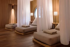 three beds with white drapes on them in a room that has wood floors and wooden walls