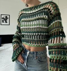 a woman standing in front of a bed wearing jeans and a crop top with crochet on it