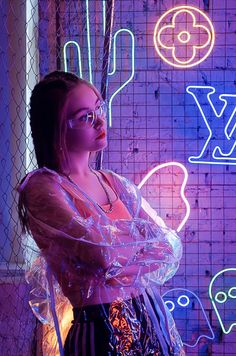 a woman standing in front of a neon sign with her arms wrapped around her body