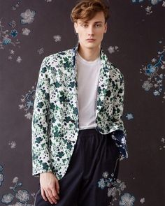 a young man is standing in front of a floral wallpaper