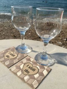 two wine glasses sitting on top of a table next to each other near the ocean