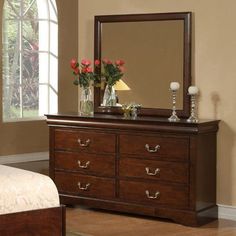 a bedroom scene with focus on the dresser and mirror in the foreground as well as flowers