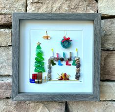 a frame with some christmas decorations in it on a stone wall next to a brick wall