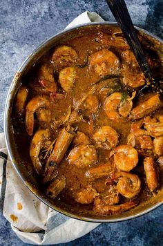 a pot filled with shrimp and sauce on top of a blue table cloth next to a wooden spoon