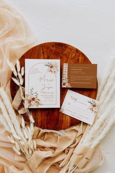 the wedding stationery is laid out on a round wooden table with dried grass and flowers