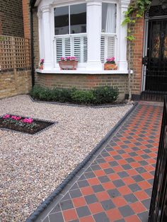 a brick walkway leading to a house with white shutters and flowers in the window boxes