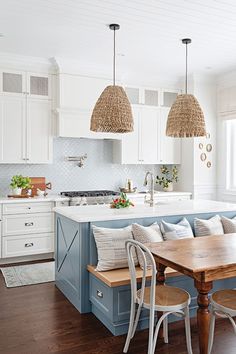 a kitchen with white cabinets and blue island in the center, surrounded by wicker pendant lights