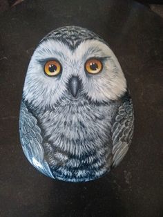 an owl painted on a rock sitting on a black counter top, with yellow eyes