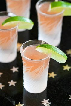 three shot glasses filled with pink lemonade and lime garnish on a black surface