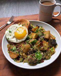 a white bowl filled with food next to a fork and cup of coffee on top of a wooden table