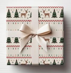 a present wrapped in white paper with reindeers and trees on it