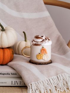 a cup of hot chocolate with whipped cream on top and pumpkins in the background