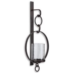 an iron candle holder with a glass hanging from it's center and two rings on the wall