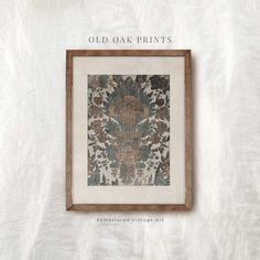 an old oak framed print with flowers and leaves on white fabric, hanging in a wooden frame