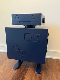 a blue robot is sitting on top of a wooden floor in front of a white wall