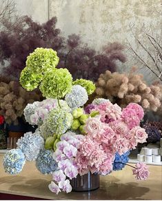 a vase filled with lots of colorful flowers on top of a wooden table in front of a painting