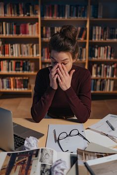 a woman sitting at a table in front of a laptop computer with her hands on her face