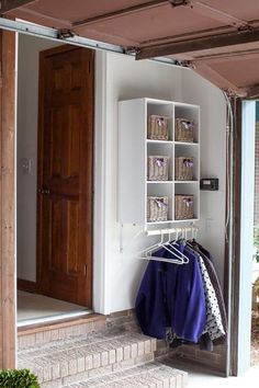 an open closet with clothes hanging on the rails and baskets in front of it, next to a door