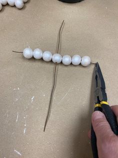 a person cutting beads with a pair of pliers on top of the table next to them