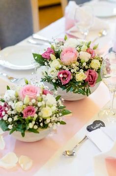 two white bowls with pink and white flowers are sitting on a table set for an event