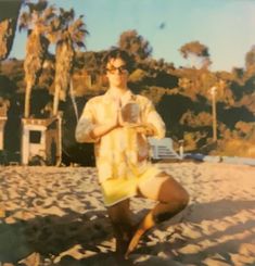 a man sitting on the beach with his legs crossed and hands folded in front of him