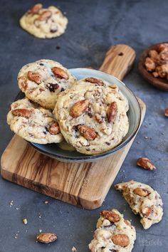 chocolate chip cookies with pecans scattered around them on a wooden cutting board next to other cookies