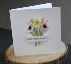 an anniversary card with flowers on it sitting on top of a piece of tree stump