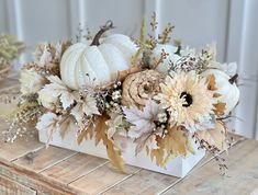 an arrangement of flowers and pumpkins in a white vase on a wooden table top