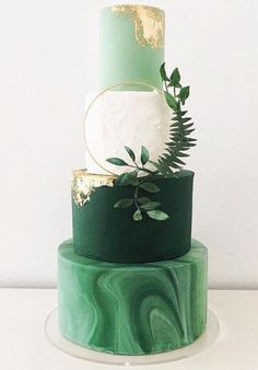 a three tiered green and gold wedding cake with greenery on the top layer