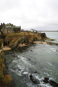 an old castle sitting on top of a cliff next to the ocean with waves coming in