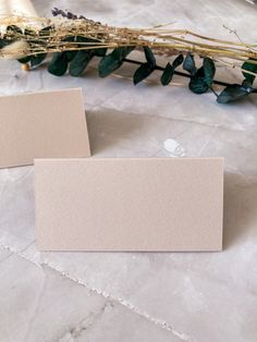 two blank cards sitting on top of a table next to flowers and greenery in front of them