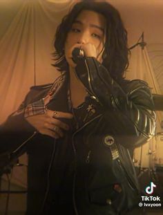 a young man singing into a microphone while wearing a black leather jacket and plaid shirt