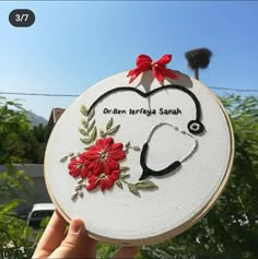 a hand holding up a embroidery hoop with a stethoscope and flowers on it