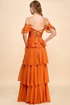 a woman wearing an orange dress with ruffles on the bottom and back, looking down