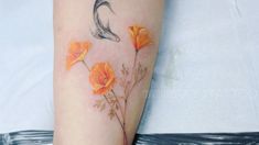 a woman's arm with orange flowers and a bird tattoo on the left forearm