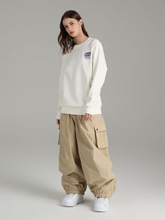 a woman in white sweatshirt and khaki cargo pants standing against a gray background