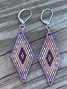 two pairs of purple and yellow beaded earrings on wooden table with metal hooks