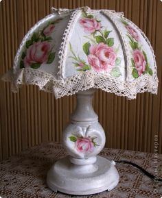 a white lamp with pink roses on it sitting on a lace doily table cloth