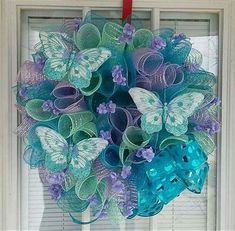 a wreath hanging on the front door with butterflies and flowers in blue, purple and green colors