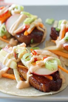 three tacos with meat, vegetables and dressing on them sitting on a white plate