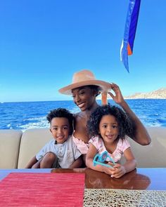 a woman and two children sitting at a table in front of the ocean on a boat