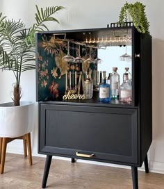 a black cabinet filled with liquor bottles and glasses sitting on top of a hard wood floor next to a potted plant