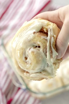 a person holding a pastry with icing in a glass dish on top of a table