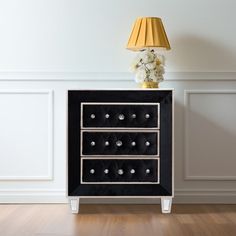 a black and white cabinet with two drawers on top of it next to a lamp