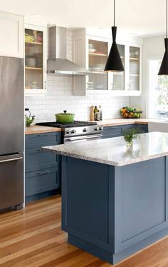 a kitchen with blue cabinets and white counter tops, an island in the middle is surrounded by black pendant lights