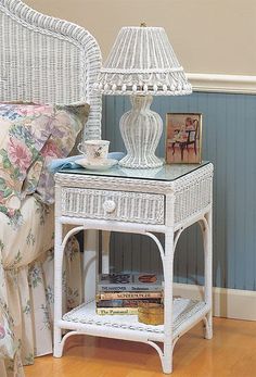 a white wicker night stand with a lamp and books on it in a bedroom